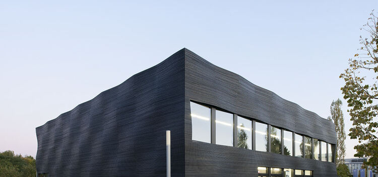 Ein markantes Gebäude mit dunkler Wellenoptik: Es steht auf dem Campus der TU München in Garching und beherbergt zwei Hörsäle fü