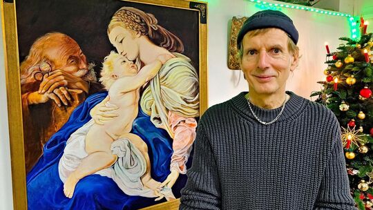 Das Foto zeigt Galerist Wolfgang Diez neben seinem Gemälde „Heilige Familie“, das er nach einem berühmten Vorbild aus dem 18. Ja