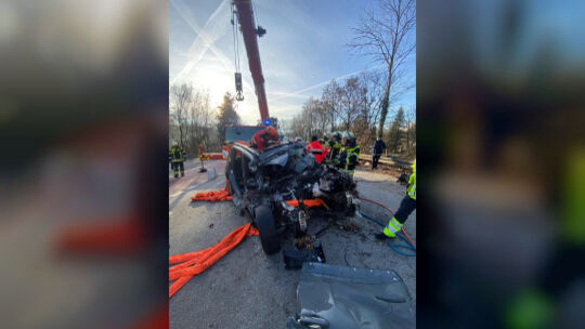 Nachdem das stark beschädigte Auto wieder auf der Straße steht, kann die Feuerwehr damit beginnen, den eingeklemmten Fahrer zu b Nachdem das stark beschädigte Auto wieder auf der Straße steht, kann die Feuerwehr damit beginnen, den eingeklemmten Fahrer zu b