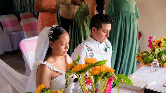In Mexiko ist der Brauch des „El Lazo“ zentral: Ein dekoratives Band oder ein großer Rosenkranz wird während der Zeremonie in Fo