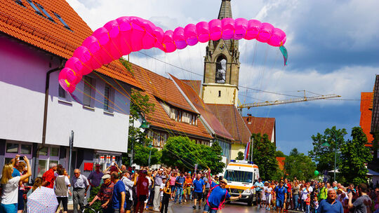 Um wirklich abzuheben hätte der Gleitschirmpilot vermutlich weit rennen müssen. Beim Umzug war der pinke Schirm jedoch eine bege Um wirklich abzuheben hätte der Gleitschirmpilot vermutlich weit rennen müssen. Beim Umzug war der pinke Schirm jedoch eine bege