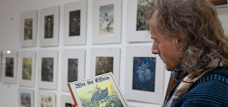 Galerist Wolfgang Diez hält vor den Originalen das Märchenbuch von Auguste Langbein-Mährlen in den Händen. Fotos: Jean-Luc Jacqu
