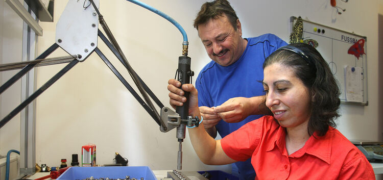 In der kleinen Werkstatt des Tageszentrums fertigt eine Besucherin mithilfe des Druckluftschraubers Klemmen. Mübin Agakay (links