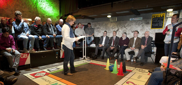 Moderatorin Gesa von Leesen erklärt die Spielregeln von „Wahlopoly“, während die fünf Kandidaten am Spielfeld gebannt lauschen (