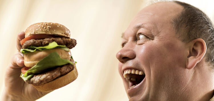 Greedy fat man holding a huge hamburger and looking at it with desire with his mouth opened.